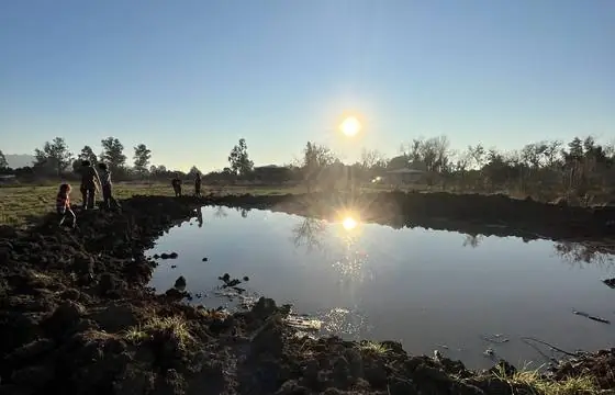 Reservorio recién excavado con agua al amanecer y personas trabajando en la orilla
